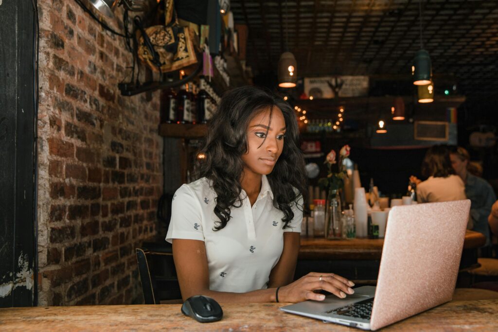 A woman focused on her laptop inside a cozy cafรฉ setting, surrounded by a warm and atmospheric interior.