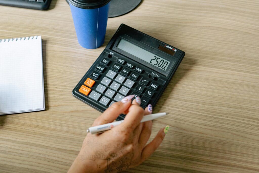 A person uses a calculator and pen on a wooden surface, focusing on office work.